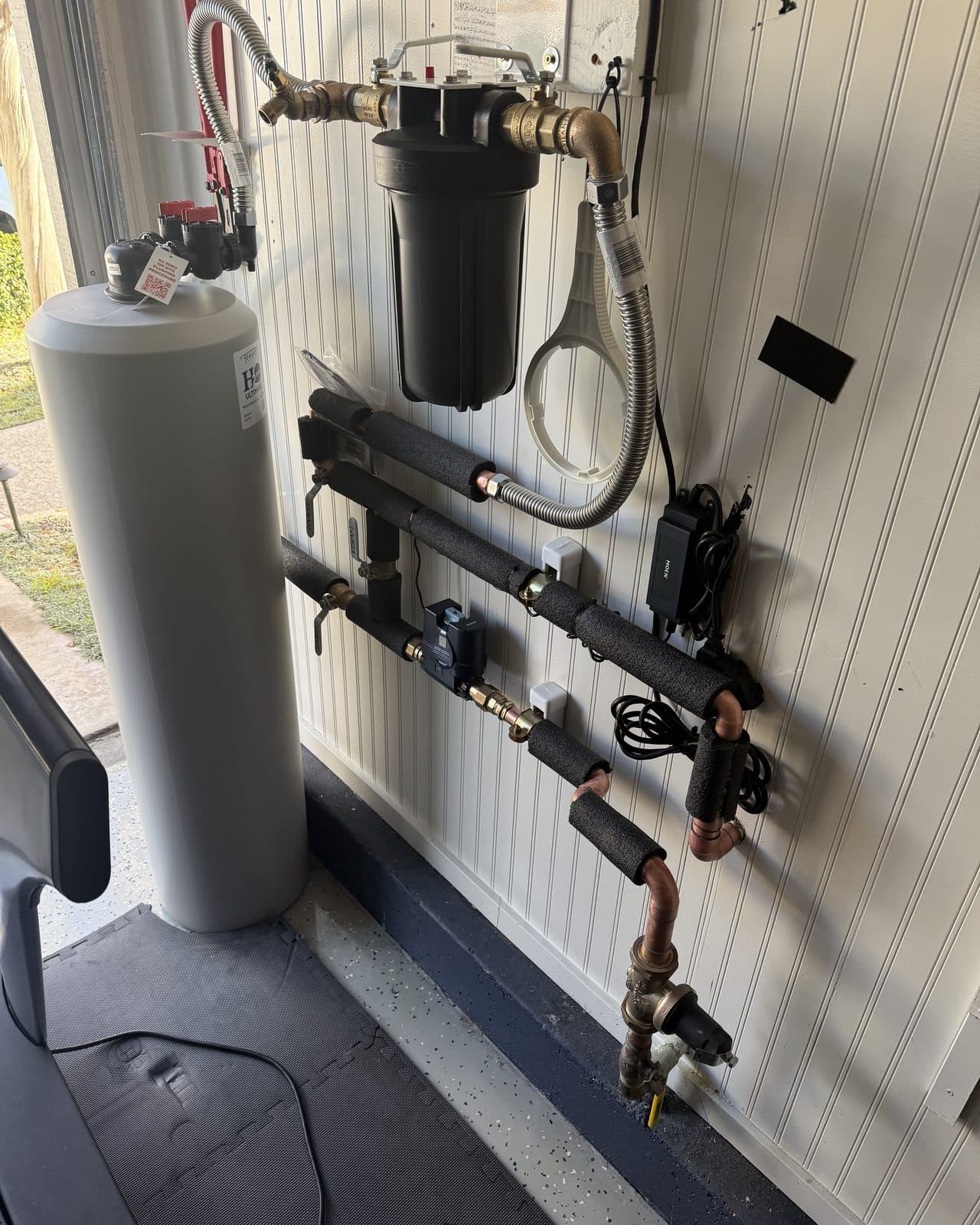Water treatment tank and filter housing plumbed to a wall manifold