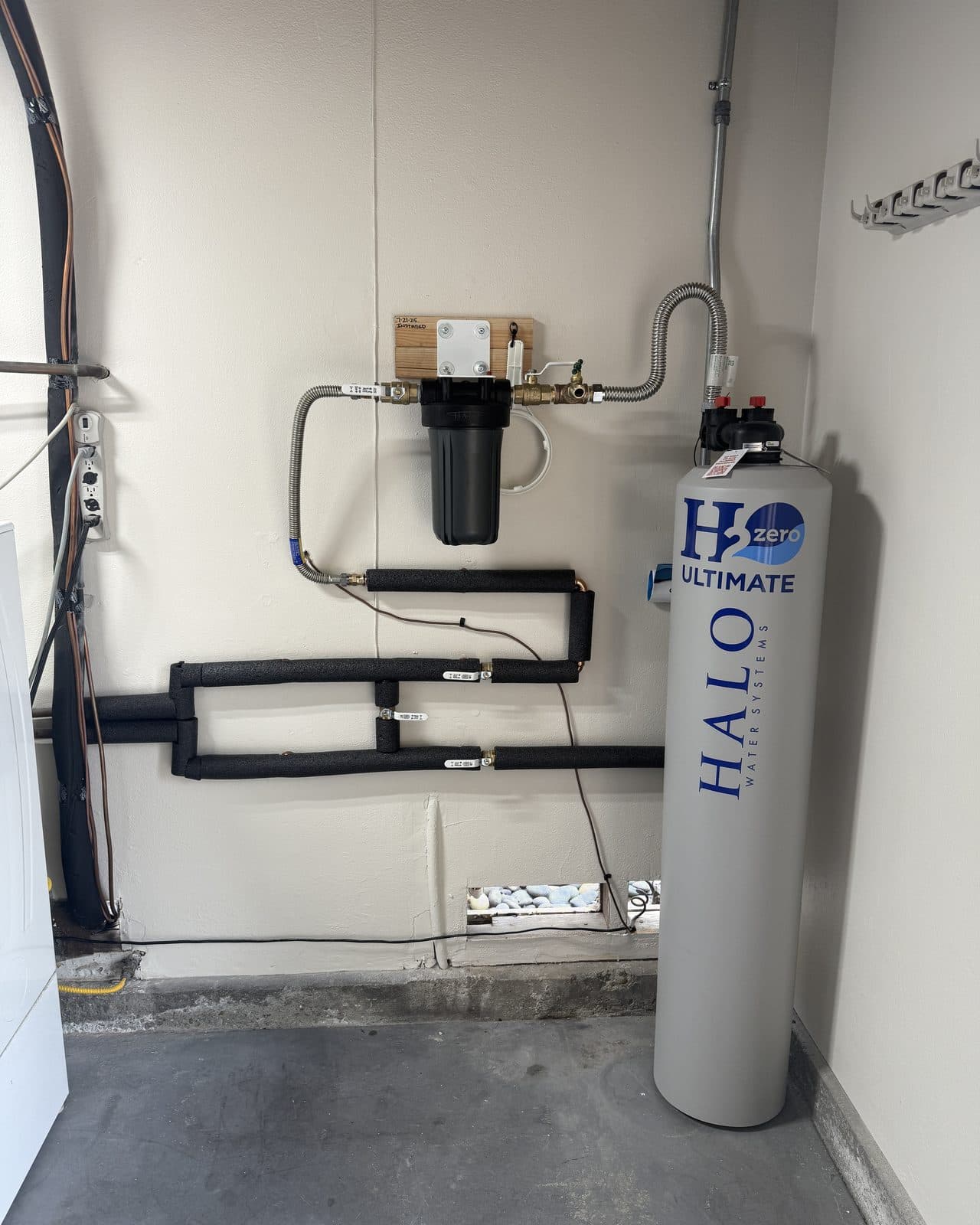 Whole house water filtration tank beside a cartridge housing on a garage wall